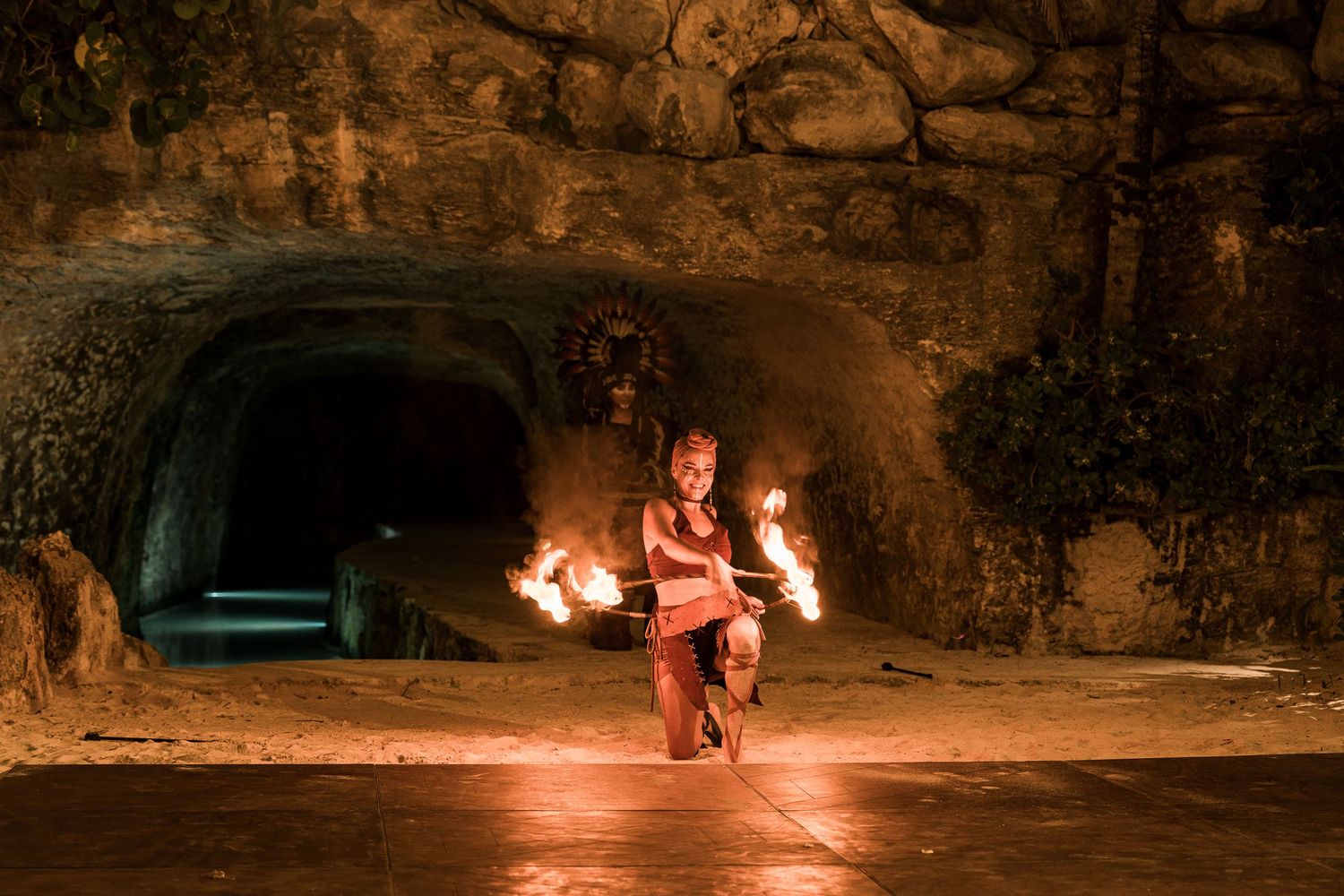 Hotel Xcaret México Fire dancer performing with flaming props inside a dramatic cave setting, illuminated by warm orange light.