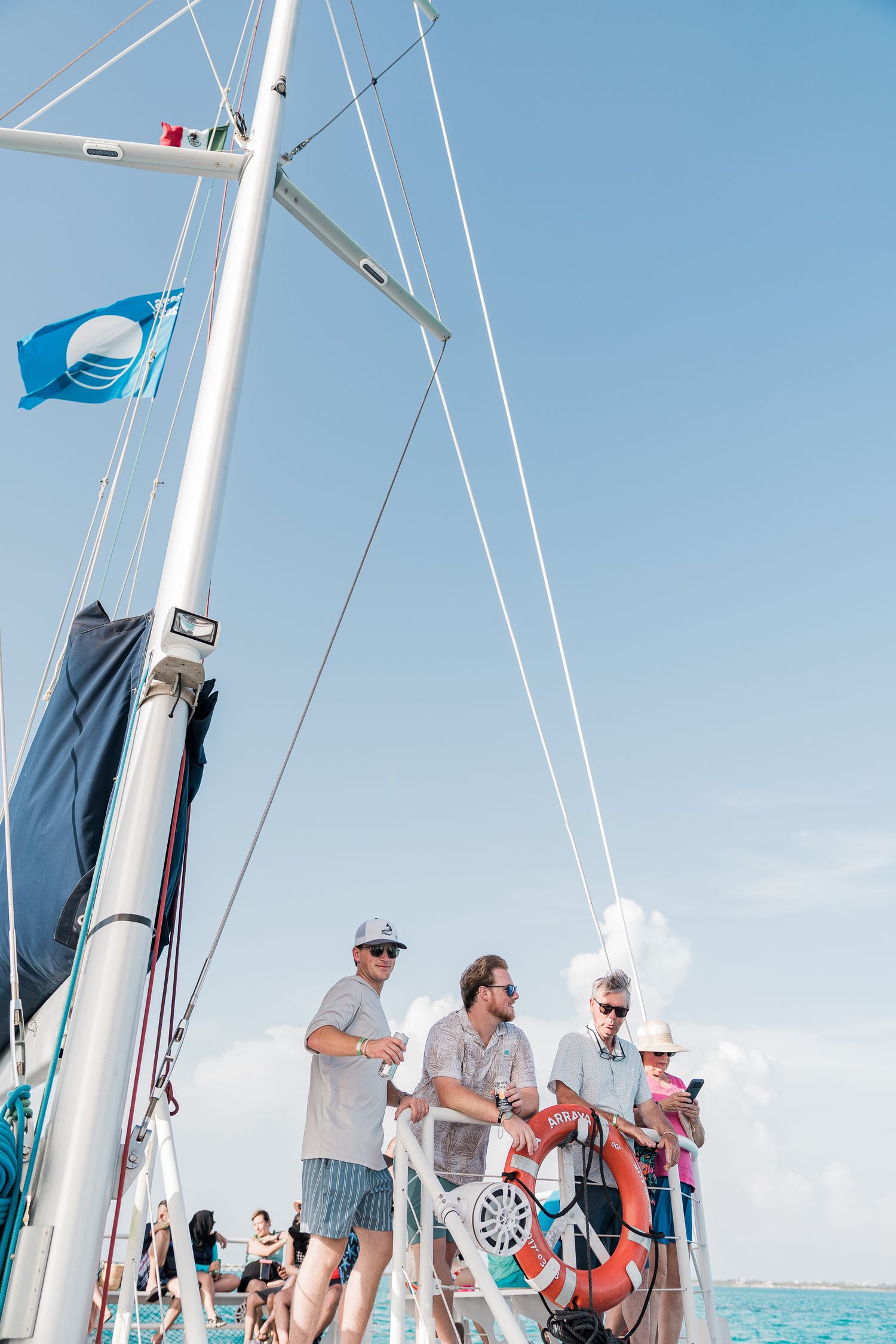 Riviera Maya Multi Day wedding - Group of people standing on a sailboat deck under blue sky, with a blue flag and life preserver visible.