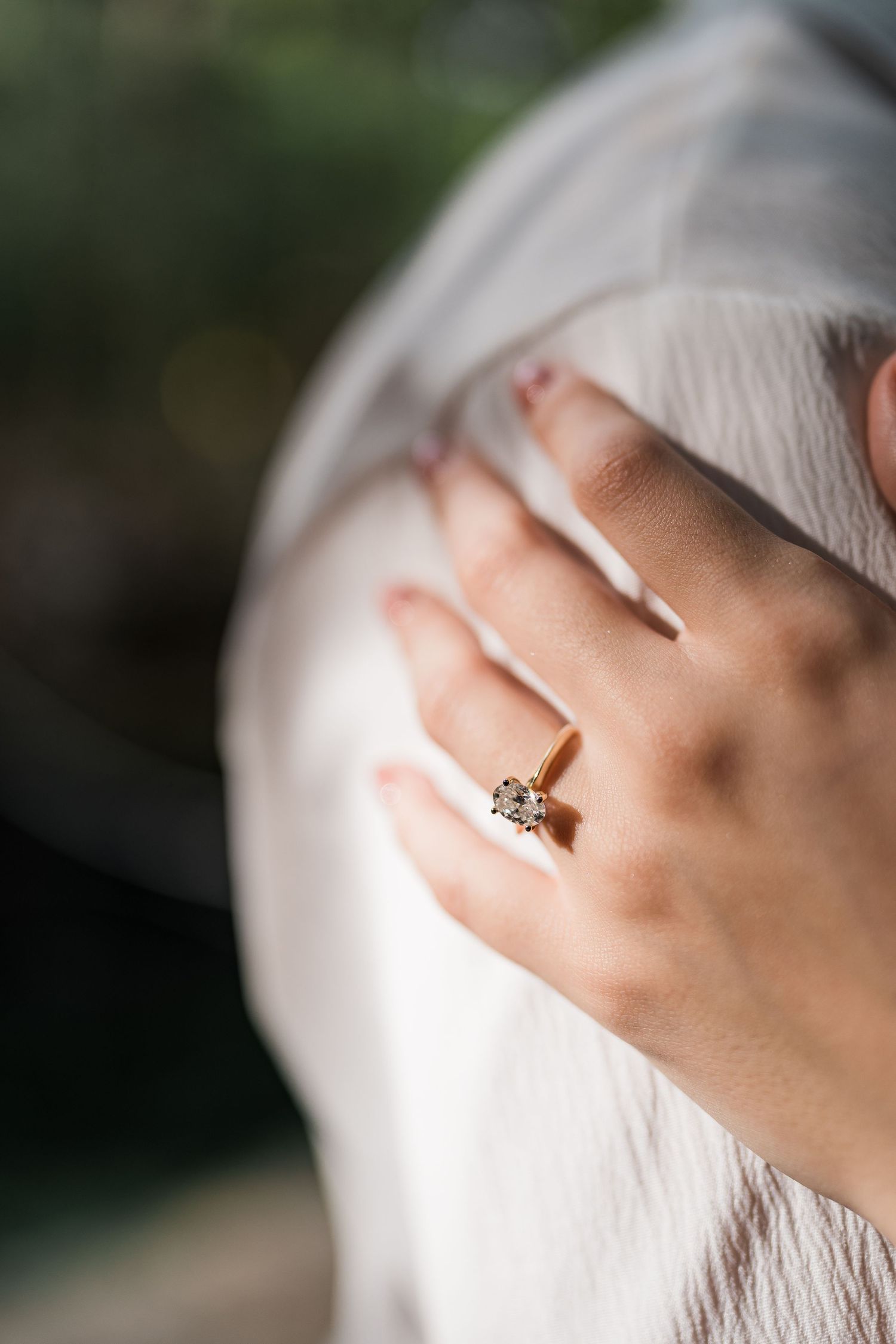 Close-up of a womans hand wearing a gold solitaire diamond engagement ring, resting on a white wedding dress.
