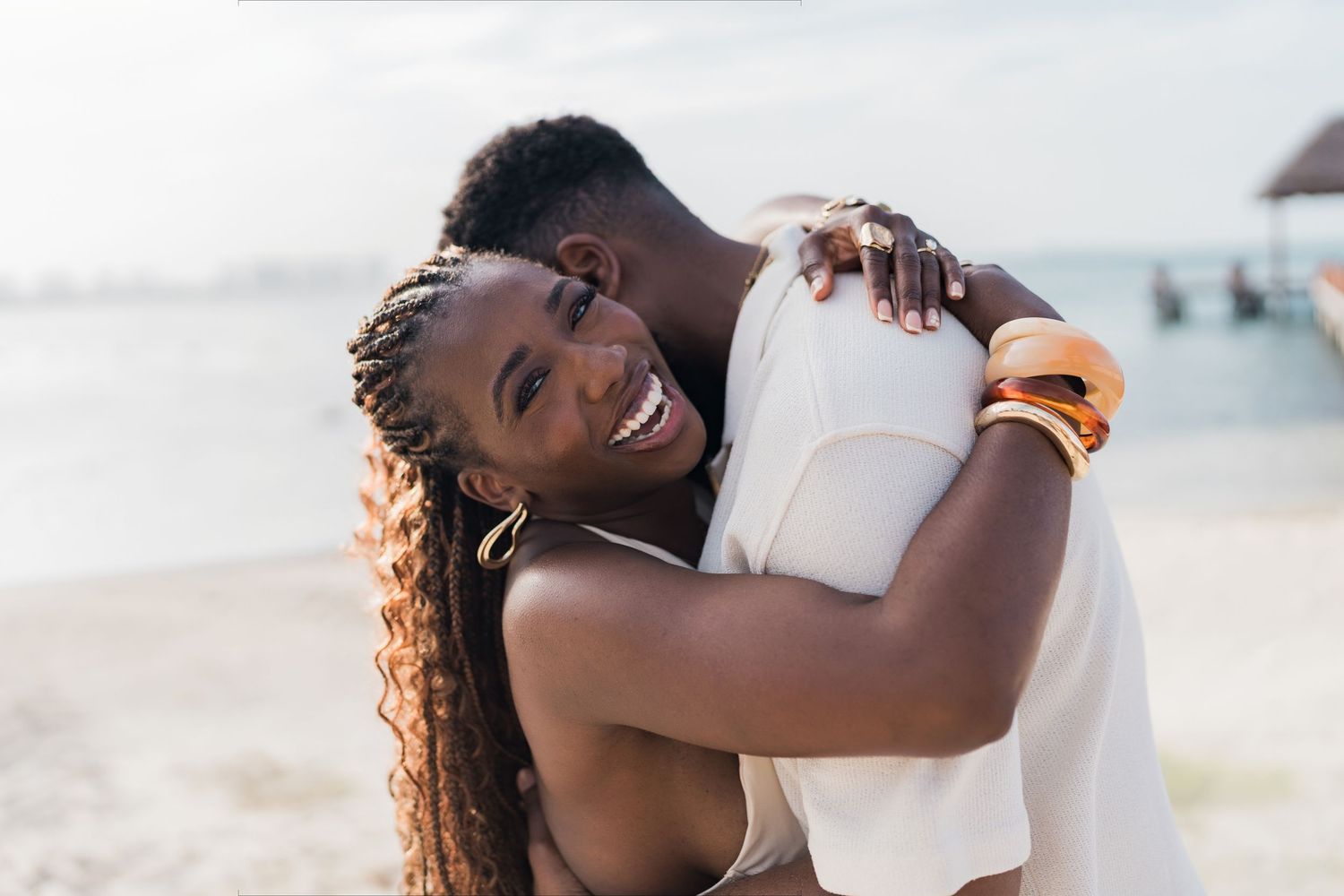 Happy Black couple embracing on a sunny beach, woman smiling with braids and orange bracelet.