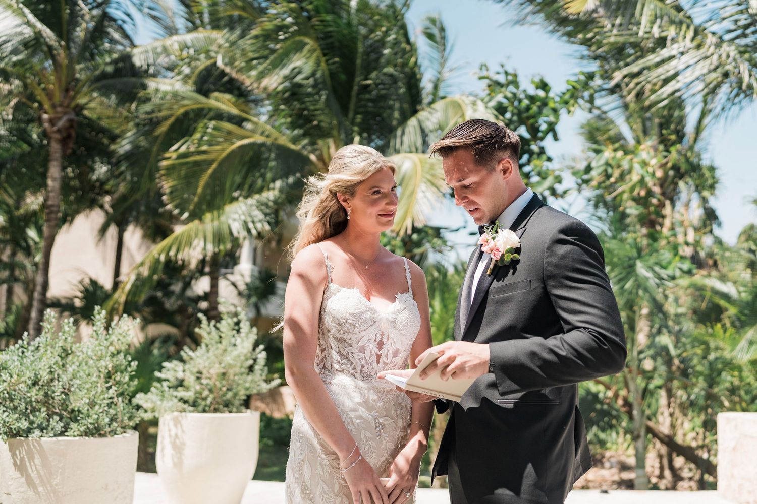 Bride and groom exchanging rings during outdoor wedding ceremony with tropical palm trees in background.