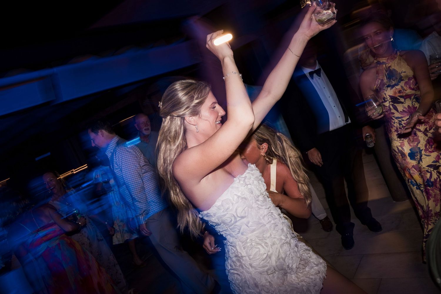 Bride in white lace gown dancing joyfully at wedding reception with guests on dimly lit dance floor. TRS Yucatán Hotel Wedding