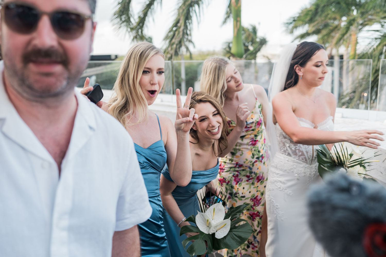 Bridesmaids in blue and floral dresses laughing and posing outdoors at a tropical wedding celebration.