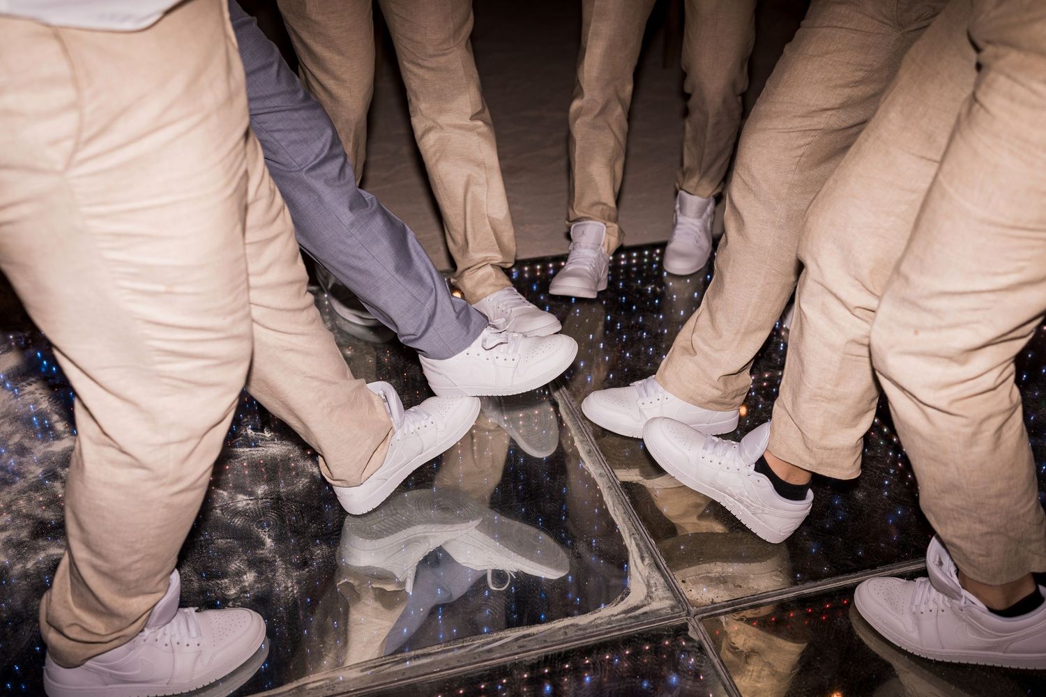 Group of people wearing beige pants and white sneakers standing together on a reflective glass floor.