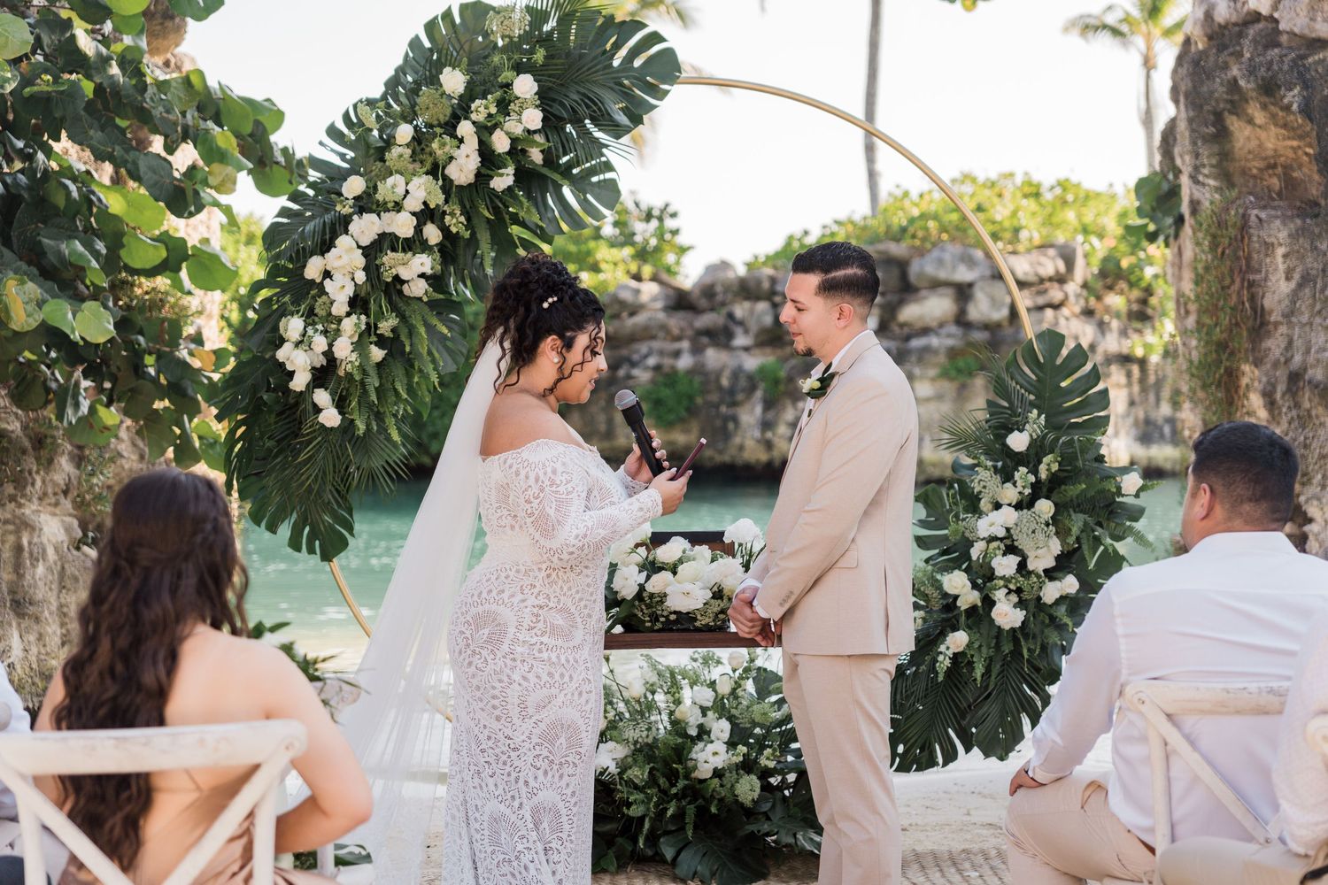 Xcaret Arte Wedding - Couple exchanging vows at tropical outdoor wedding ceremony with floral arch