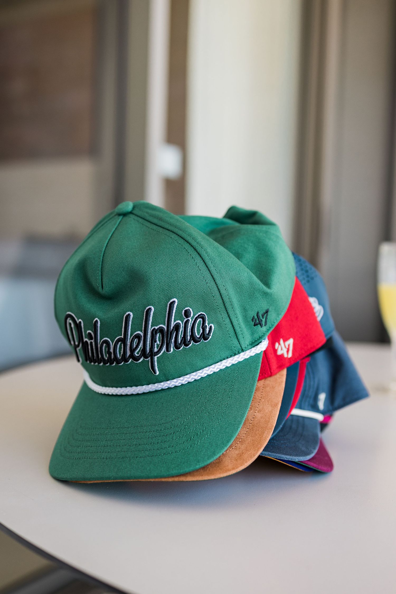 Stack of Philadelphia 47 brand snapback hats in green, red, and blue displayed on a white surface.
