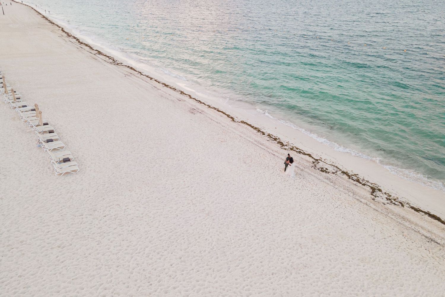 Aerial drone shot of a lone figure in wedding dress walking along a stunning white sandy tropical beach.