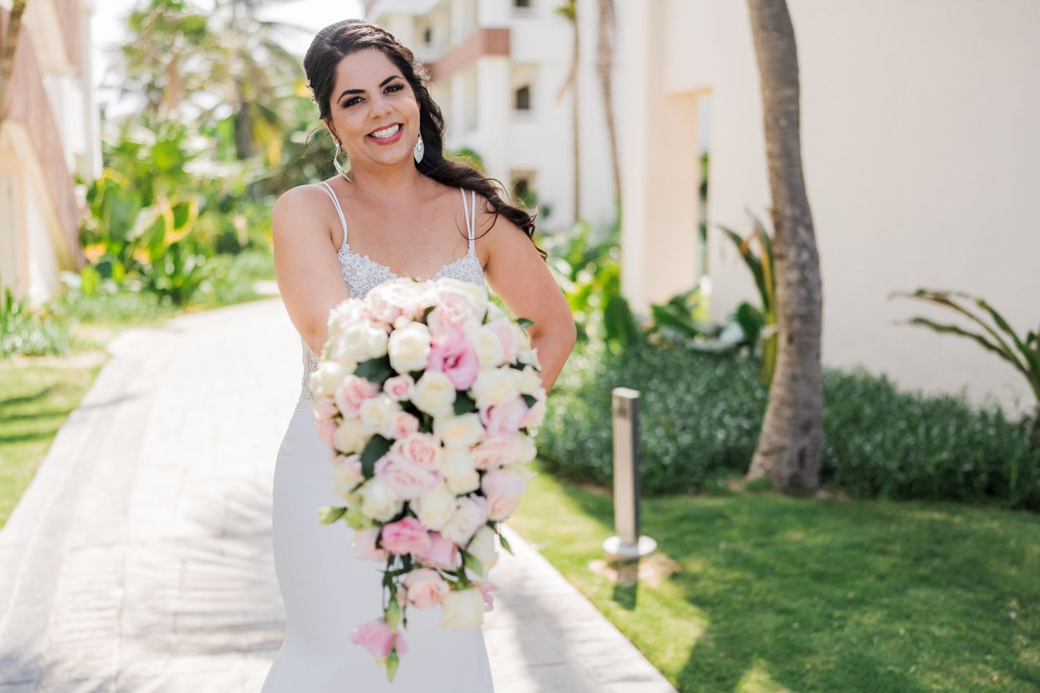 Radiant bride in spaghetti strap wedding dress holding large cascading pink and white rose bouquet.