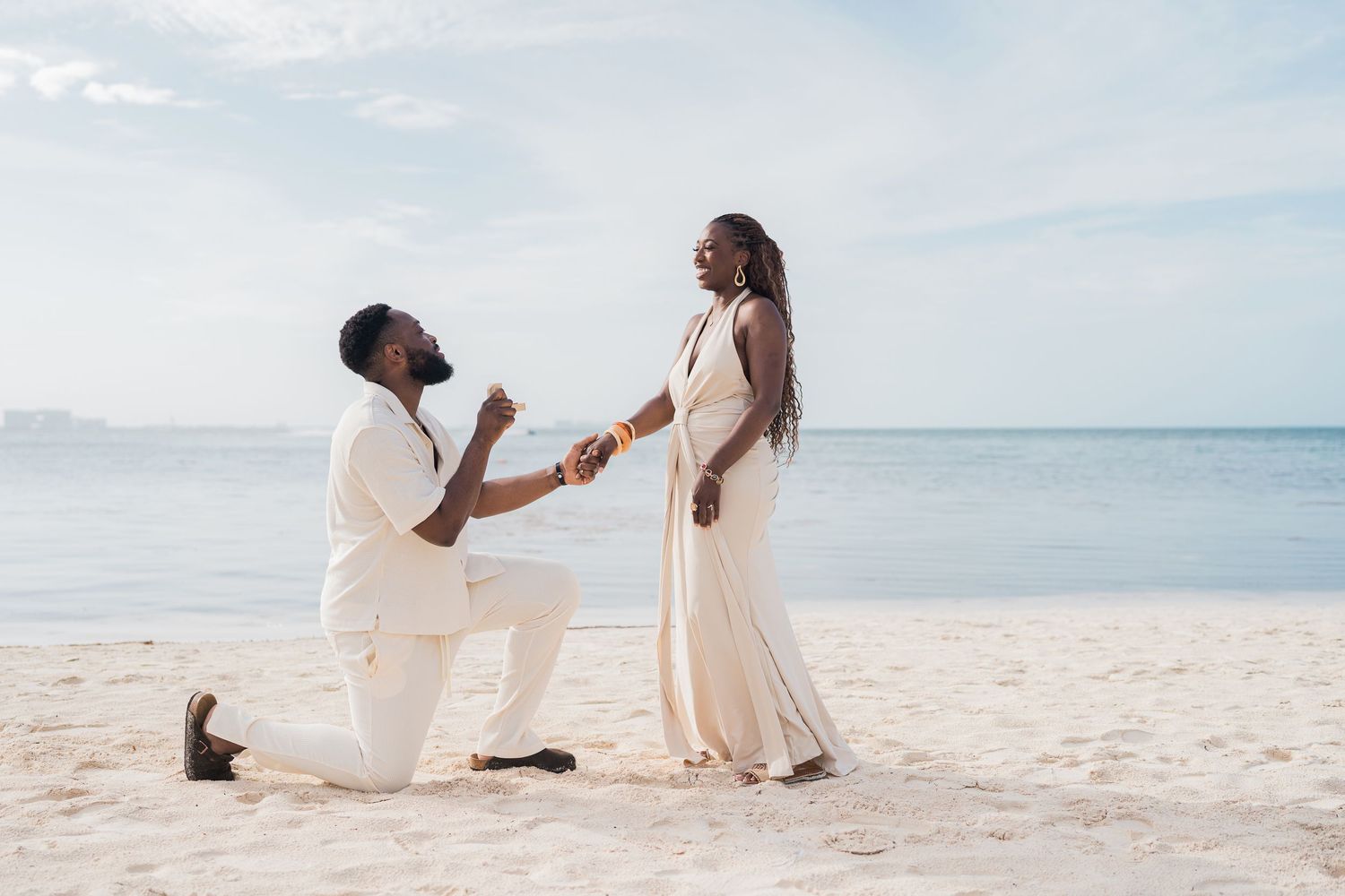 Couple sharing romantic beach proposal moment, man on one knee presenting ring to smiling woman.