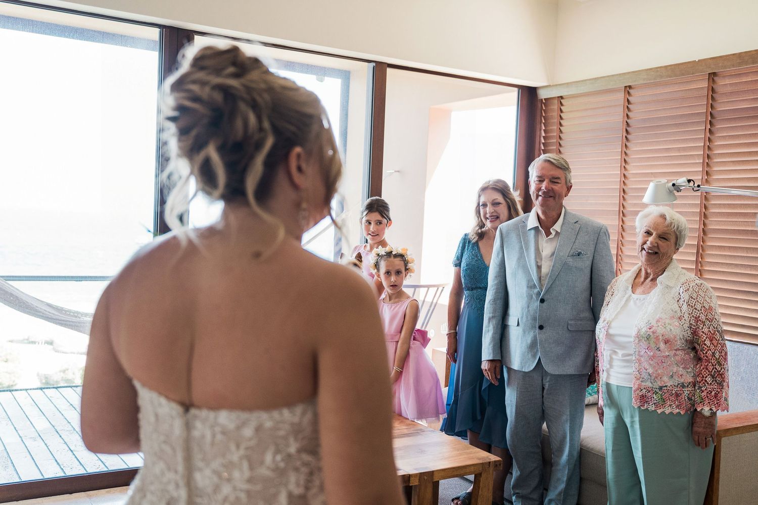 Bride in white gown shares emotional first look moment with smiling family members in elegant wedding venue.