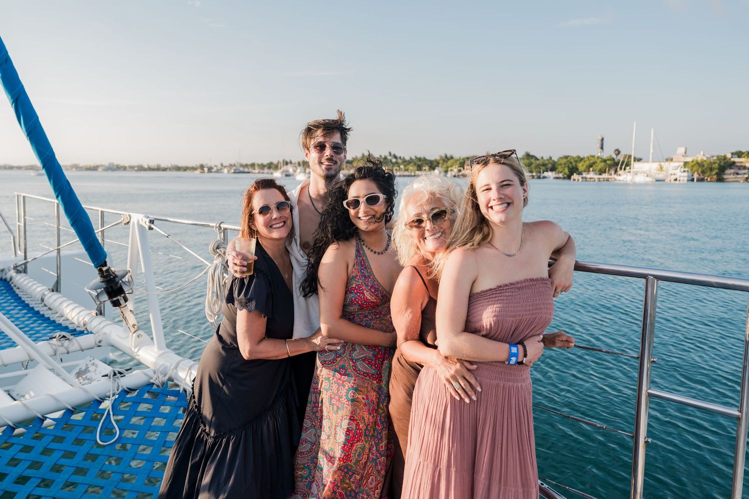 Group of friends posing together on a boat deck with scenic blue water and marina in the background.