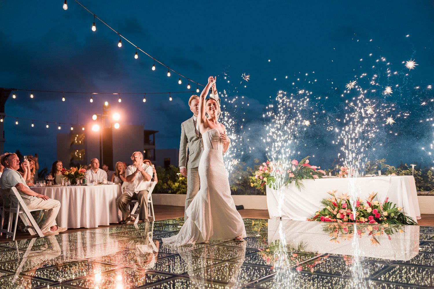 Bride and groom share first dance on mirrored floor with sparkling fireworks at elegant outdoor wedding reception.