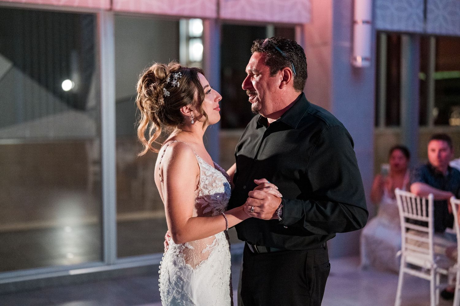 Bride shares a tender father-daughter dance, both smiling warmly in elegant wedding reception setting.