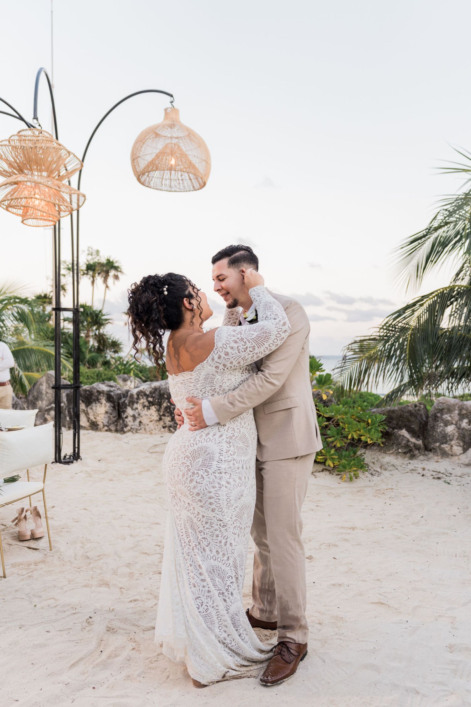 Xcaret Arte Wedding - Bride and groom share first dance on sandy beach at sunset, surrounded by boho rattan lanterns and tropical palms.