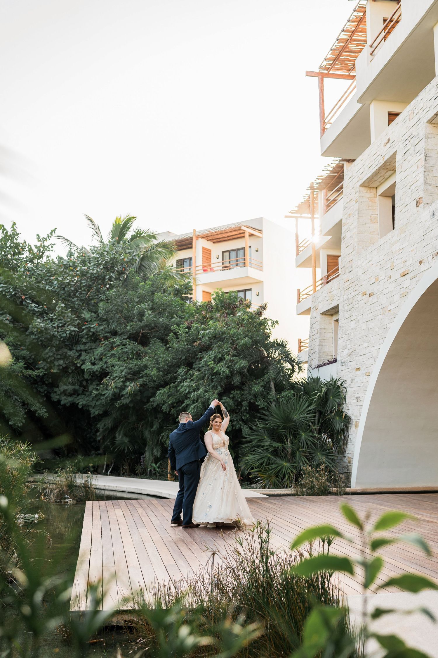 Secrets Akumal Wedding - Bride and groom dancing on a wooden deck surrounded by lush greenery and a luxury resort building.