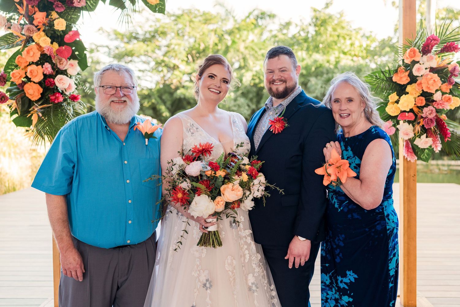 Secrets Akumal Wedding - Wedding couple with family posing outdoors near floral arch with colorful orange and red blooms.