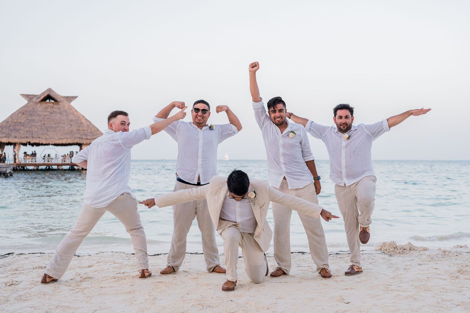 Groomsmen celebrating and jumping on tropical beach at sunset.