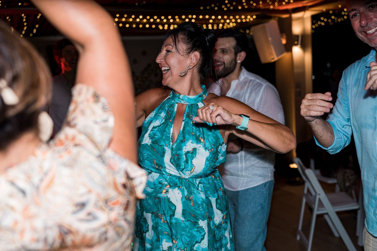 Joyful woman in green floral dress dancing with guests at an outdoor wedding reception.