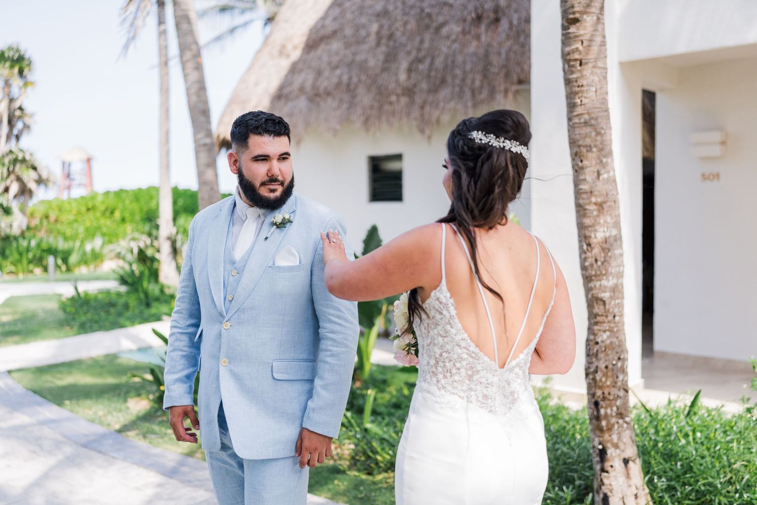 Emotional groom in light blue suit reacts during first look as bride touches his shoulder outdoors.