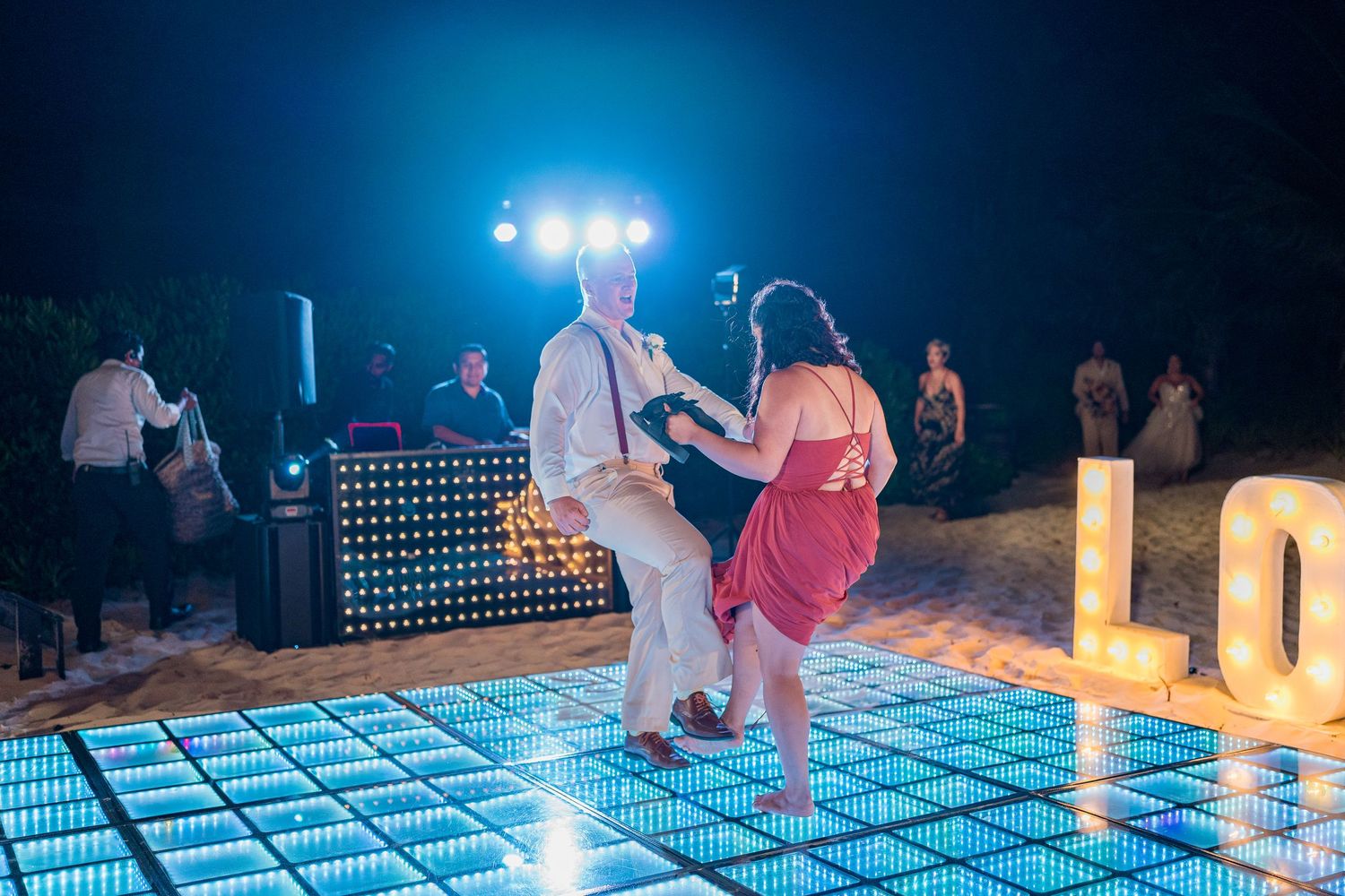 Bride and groom dancing energetically on glowing LED dance floor at outdoor beach wedding.