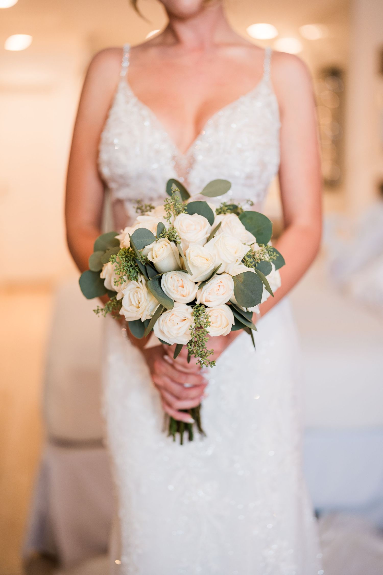 Bride in beaded gown holding elegant white rose and eucalyptus bouquet.