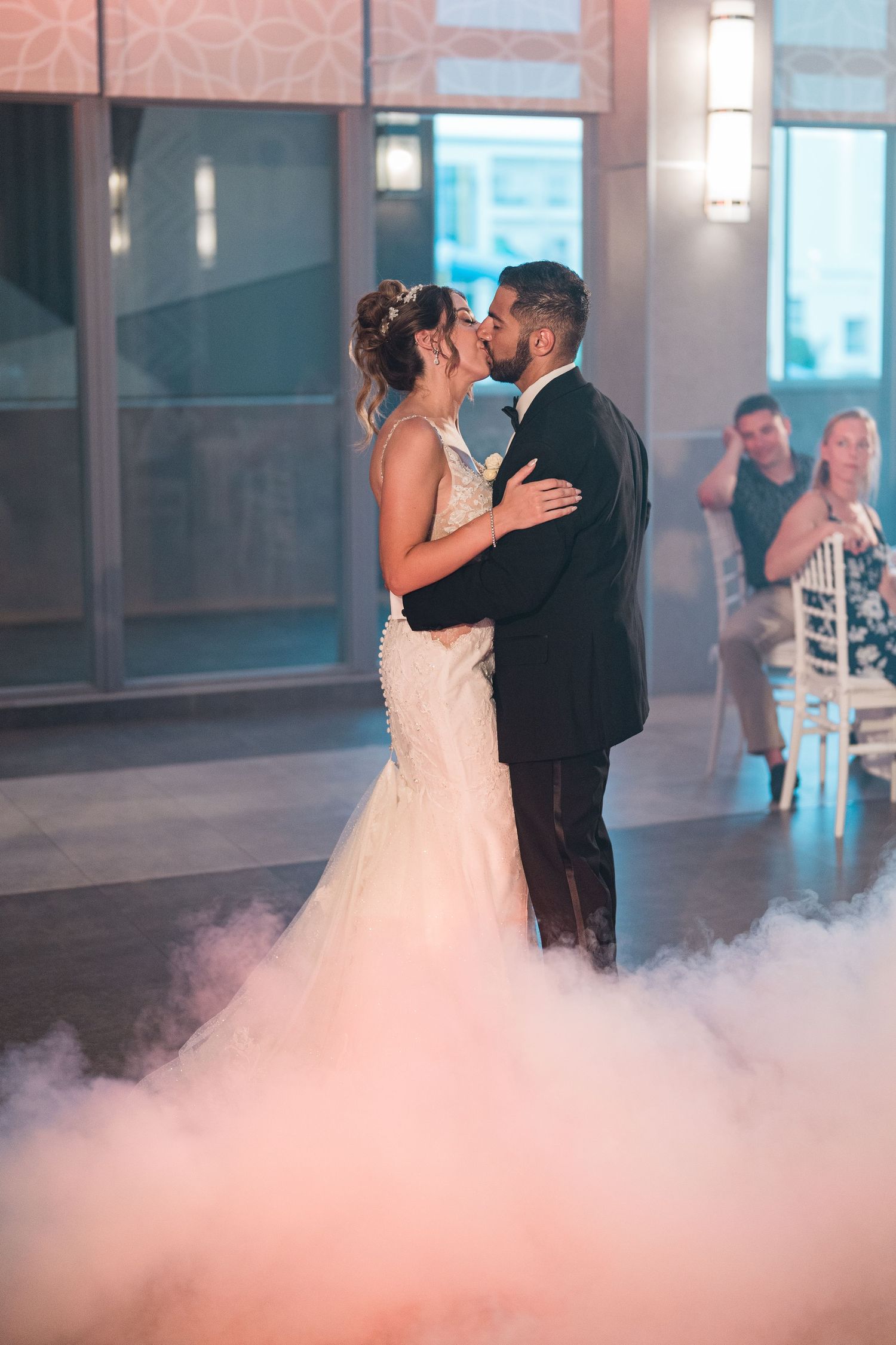 Bride and groom kiss during first dance surrounded by romantic pink fog on the dance floor.