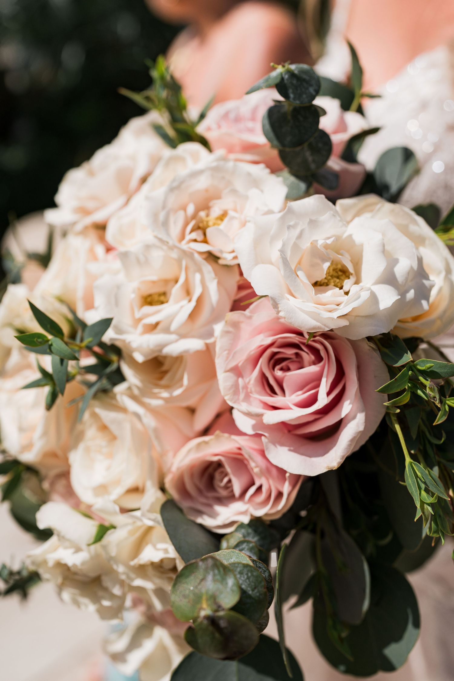 Elegant bridal bouquet featuring blush pink roses, white peonies, and eucalyptus greenery held by a bride.