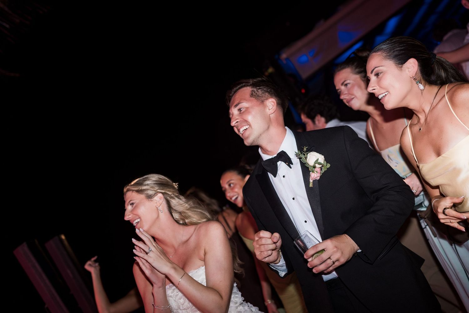 Bride and groom laughing joyfully with guests at a lively wedding reception dance floor celebration.