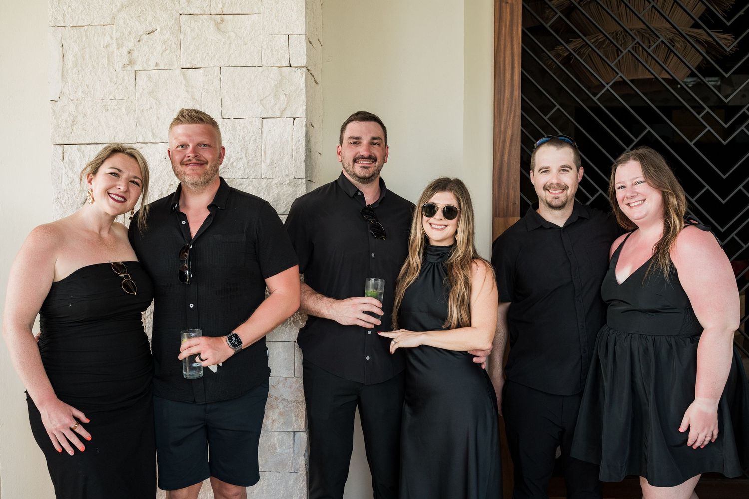 Group of six friends dressed in black posing together at an upscale venue for a formal event.