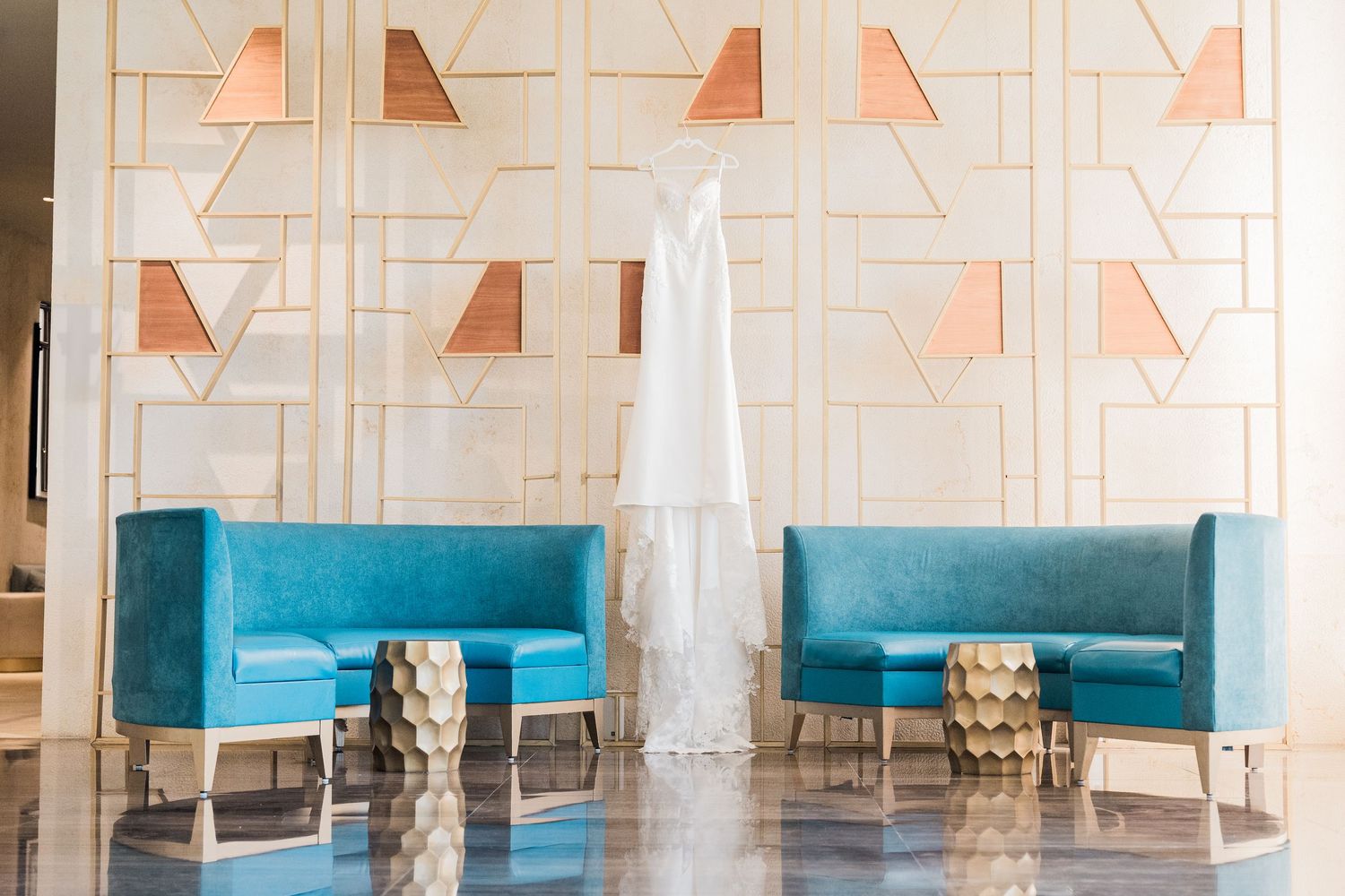 White wedding dress hanging between two teal velvet booth seats against a geometric gold and copper patterned wall.