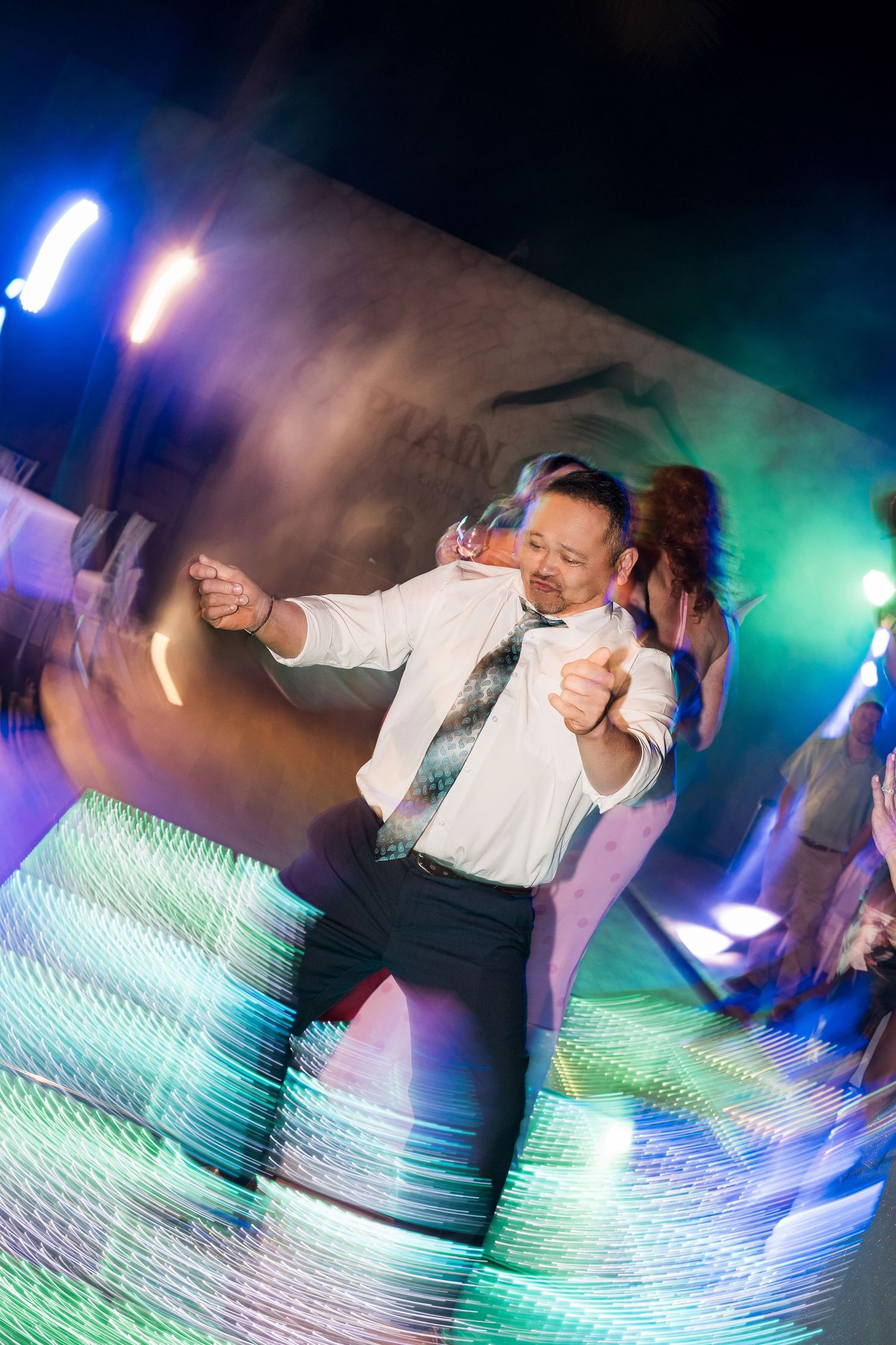 Man dancing energetically on a colorful illuminated dance floor at a nightclub party with vibrant lights.