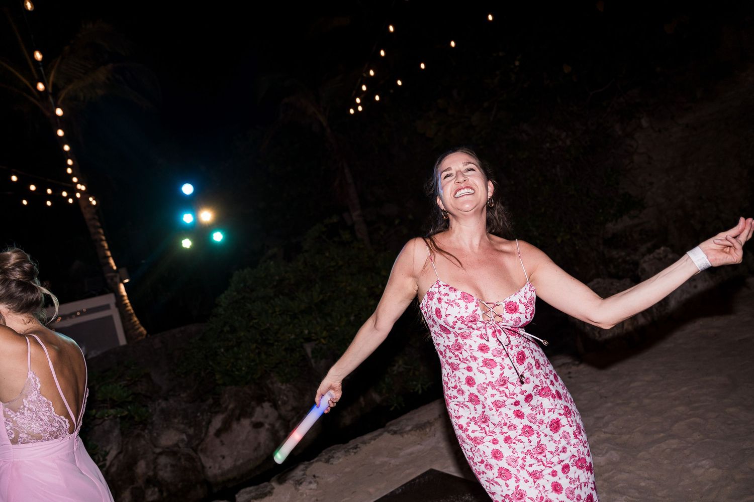 Woman in floral dress dancing joyfully at outdoor night party with string lights glowing in background.