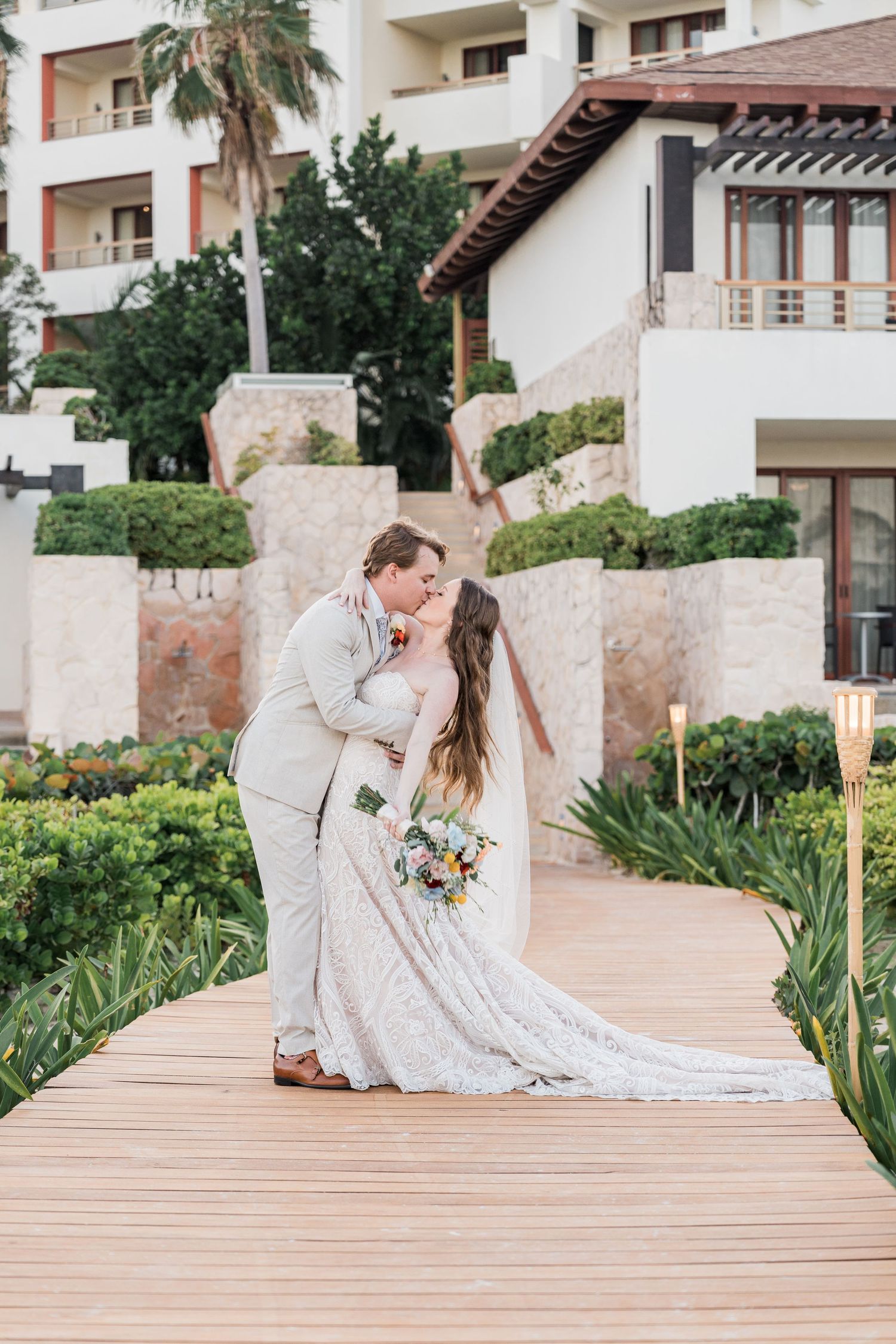 Bride and groom share a romantic kiss on a wooden walkway at a tropical resort wedding venue in Puerto Vallarta