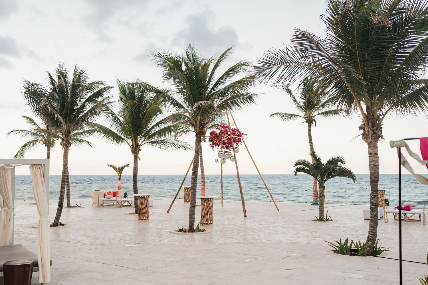 Tropical beach wedding venue with palm trees, floral arch, and ocean view on a white tiled terrace.
