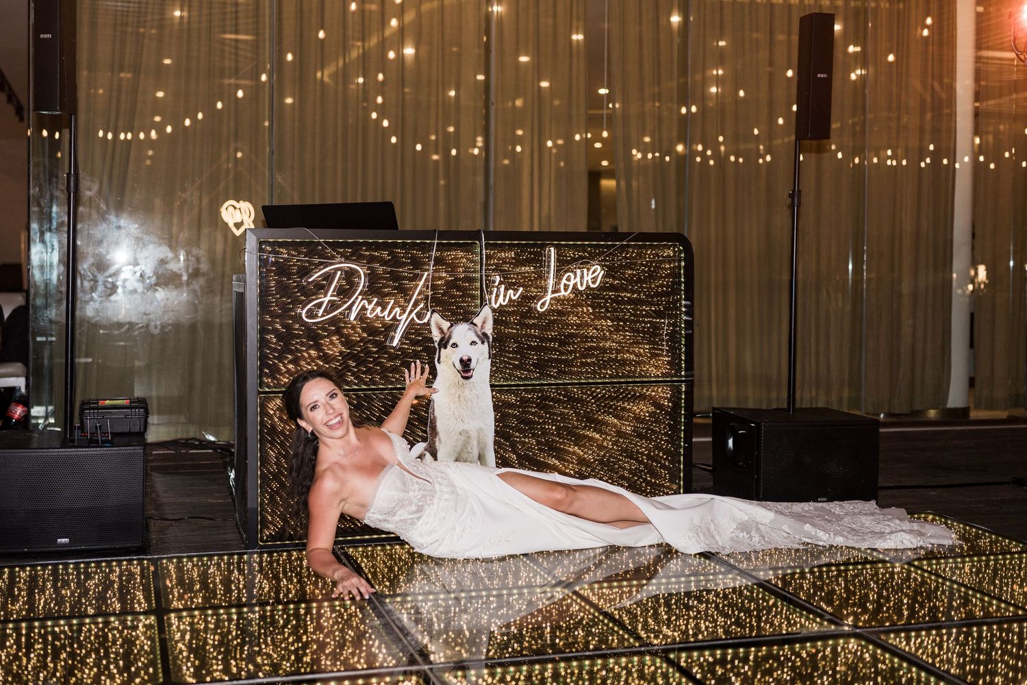Bride in white gown poses with a white llama in front of a glittering Drunk in Love neon sign backdrop.