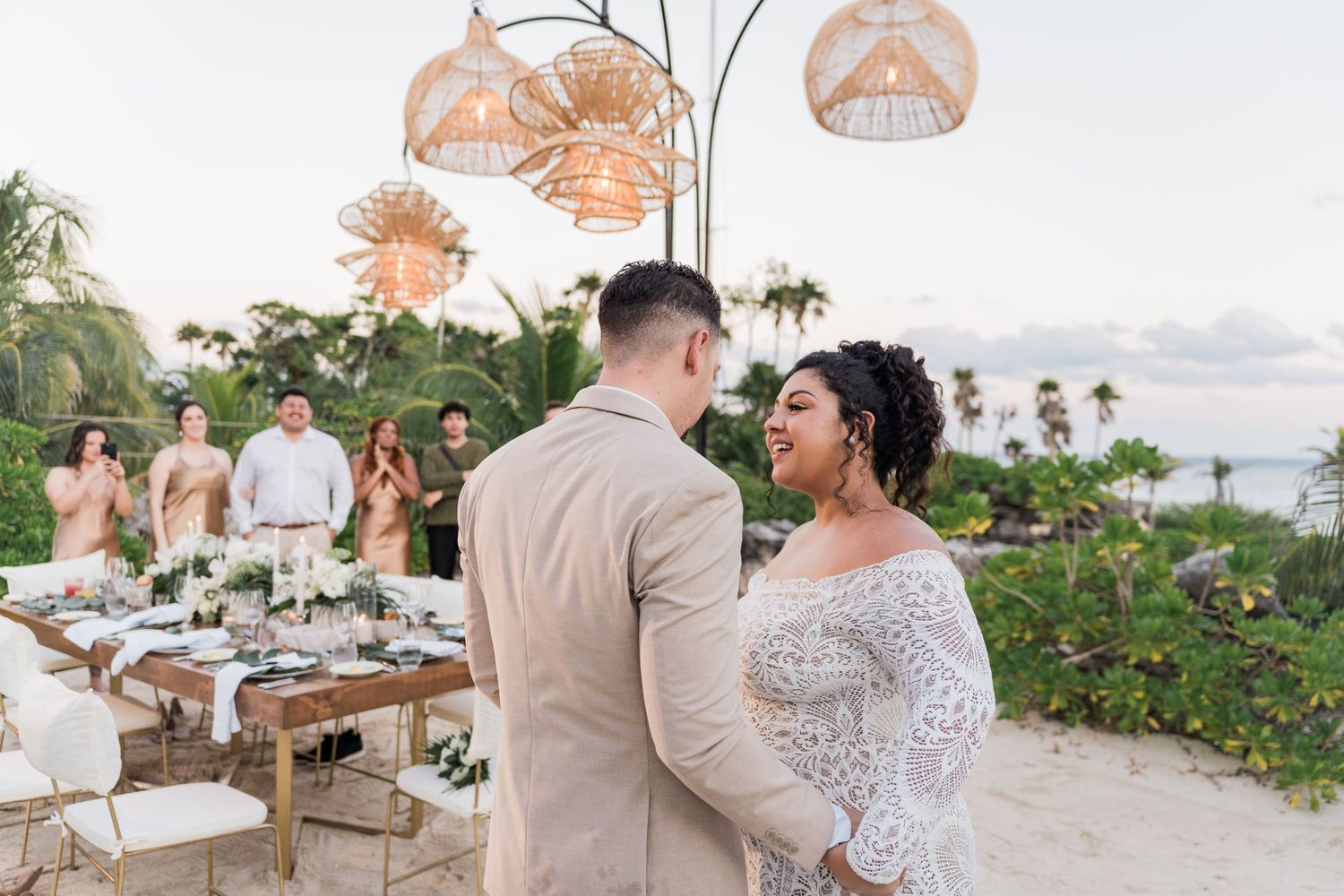 Xcaret Arte Wedding - Couple shares a romantic first dance on a beach wedding with guests and boho pendant lights at sunset.