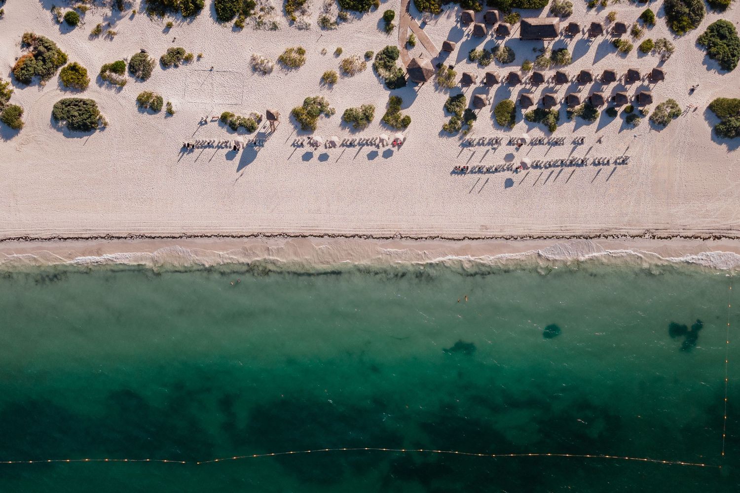 Aerial view of tropical beach with turquoise water, white sand, and thatched umbrellas.