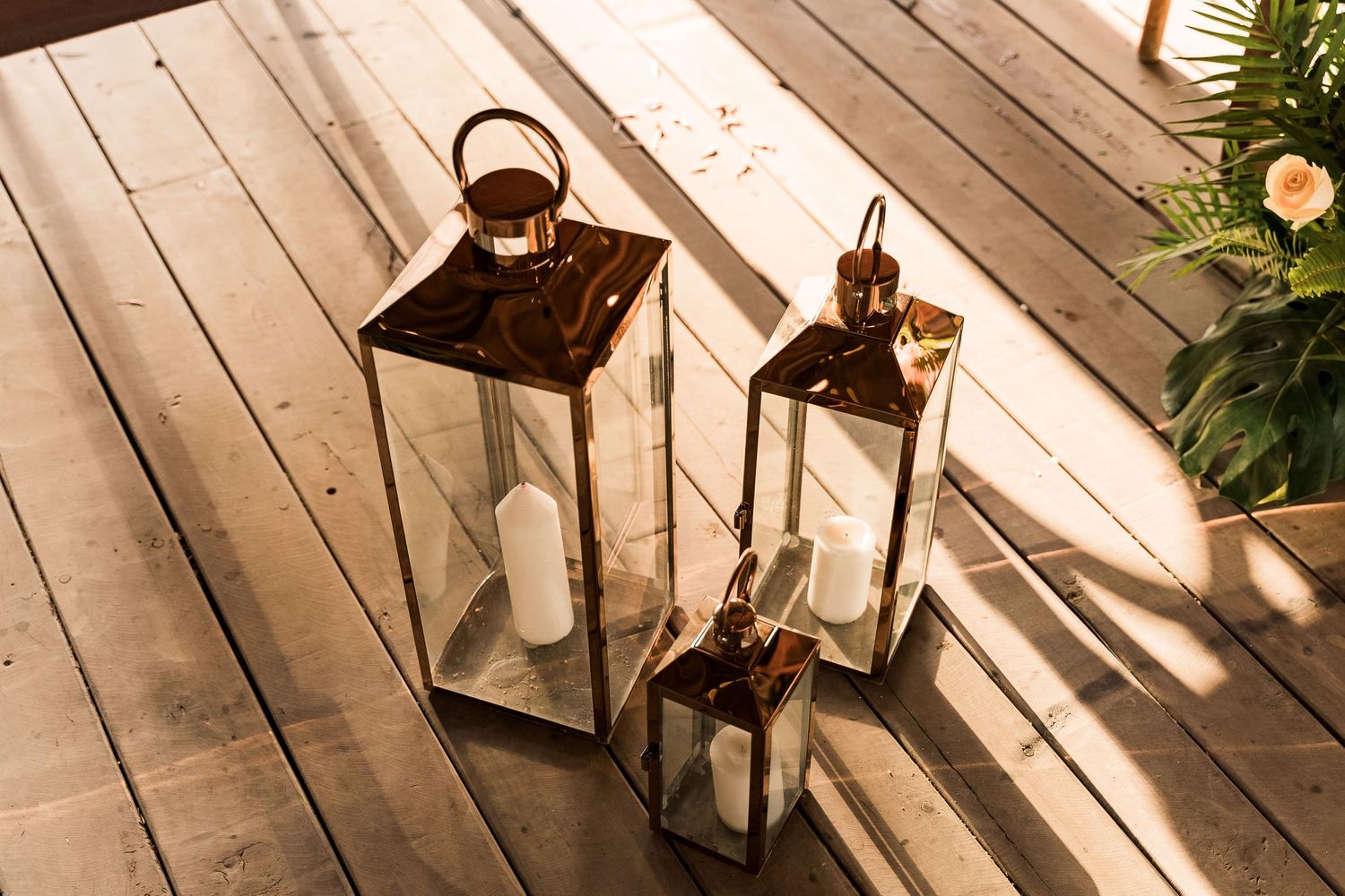 Three copper lanterns with white candles arranged on a wooden deck for a wedding reception.