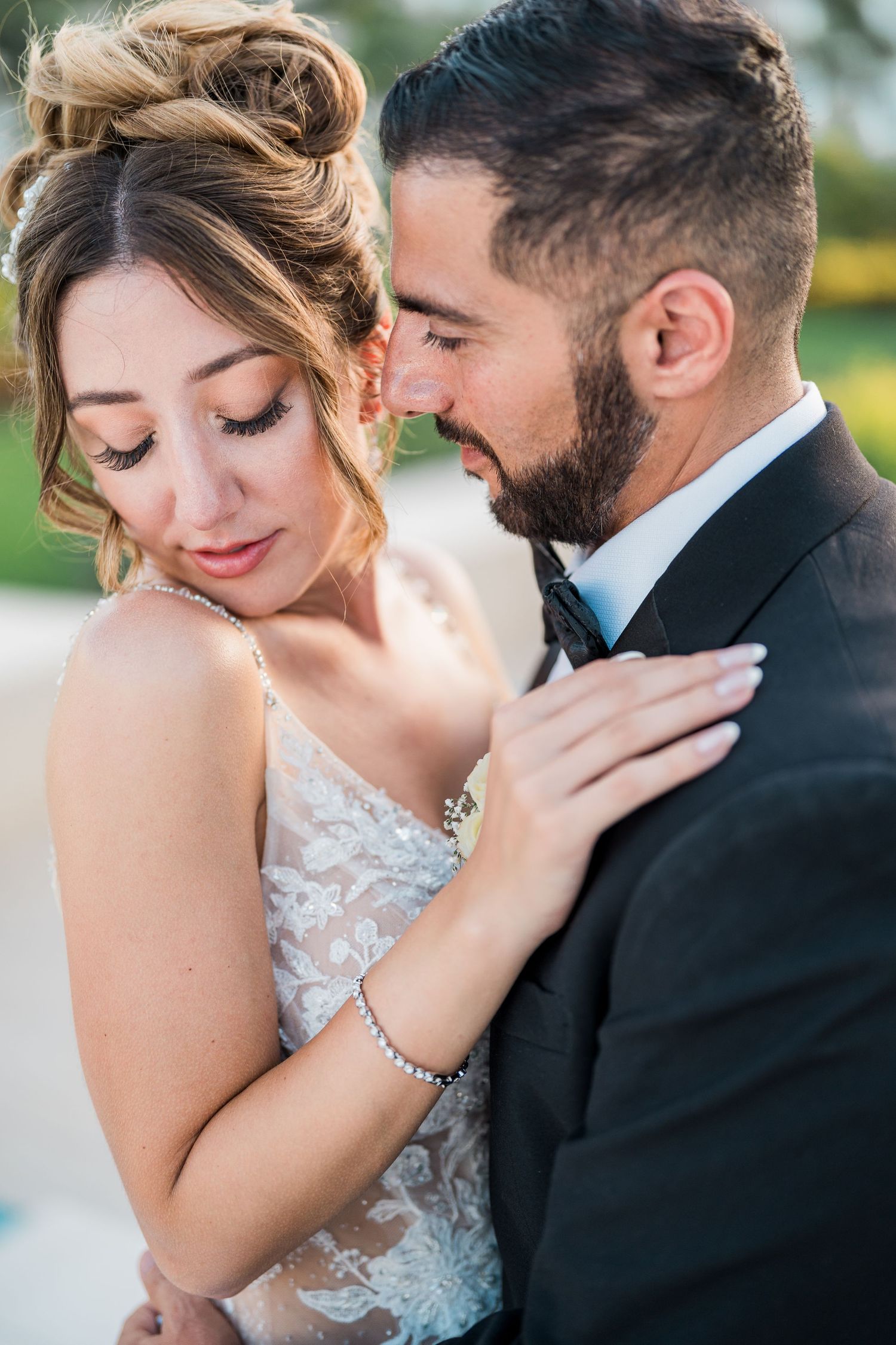 Bride and groom share an intimate forehead-to-forehead moment, bride in lace gown with updo hairstyle.