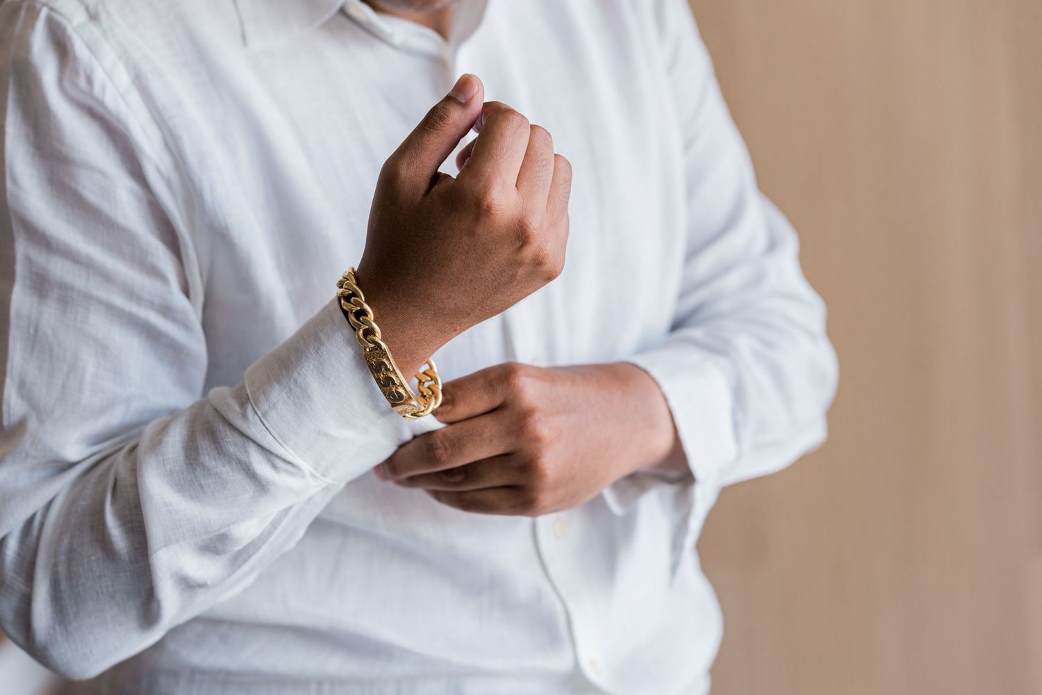 Groom adjusts gold chain bracelet on wrist while wearing white dress shirt.