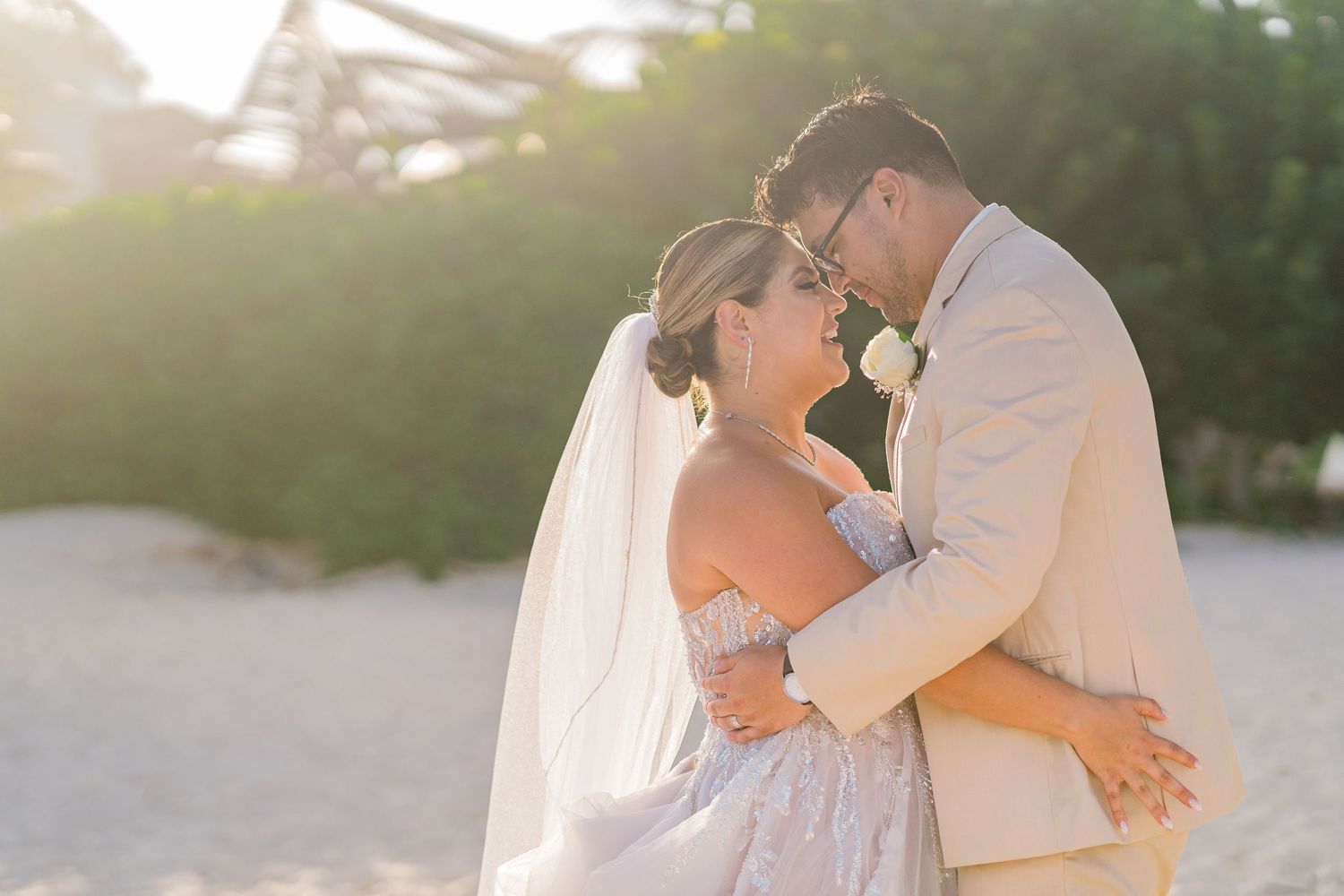 Bride and groom sharing a romantic forehead touch at golden hour on a sandy beach.