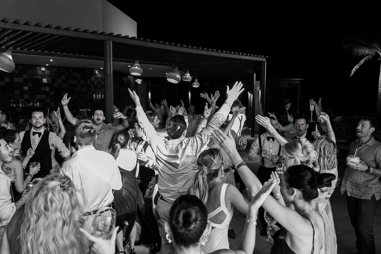 Lively wedding reception dance floor with guests celebrating, arms raised, in black and white photography.