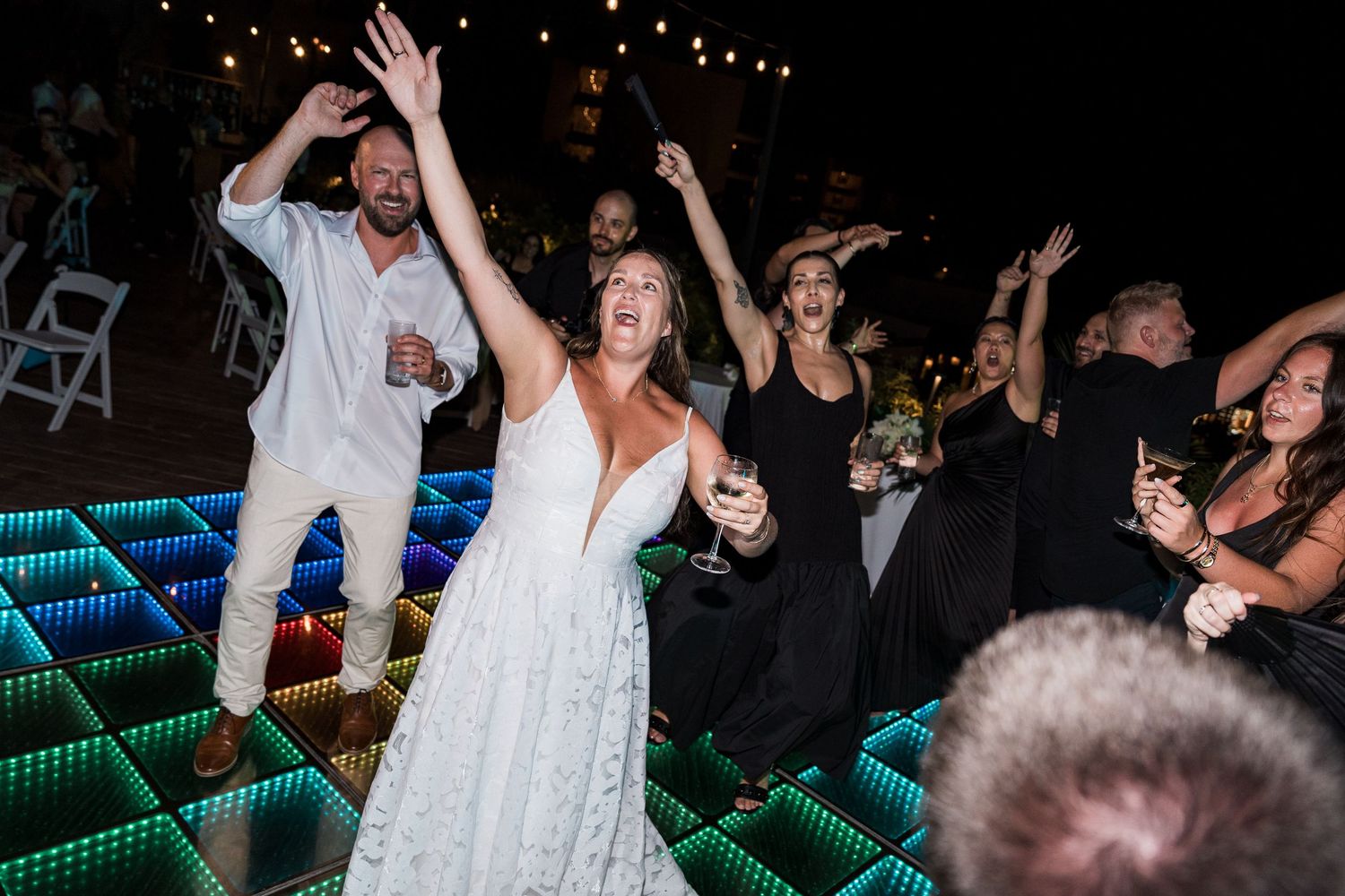 Bride and groom celebrating on illuminated LED dance floor at outdoor wedding reception at night.