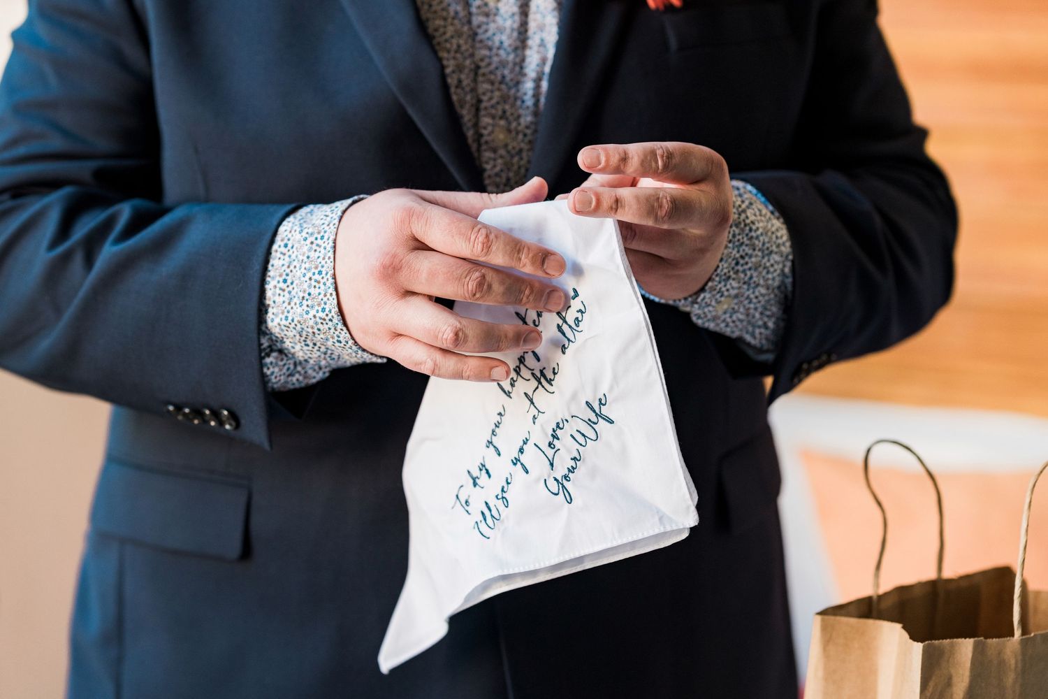 Secrets Akumal Wedding - Groom in navy suit holding a white handkerchief with handwritten calligraphy message at a wedding ceremony.