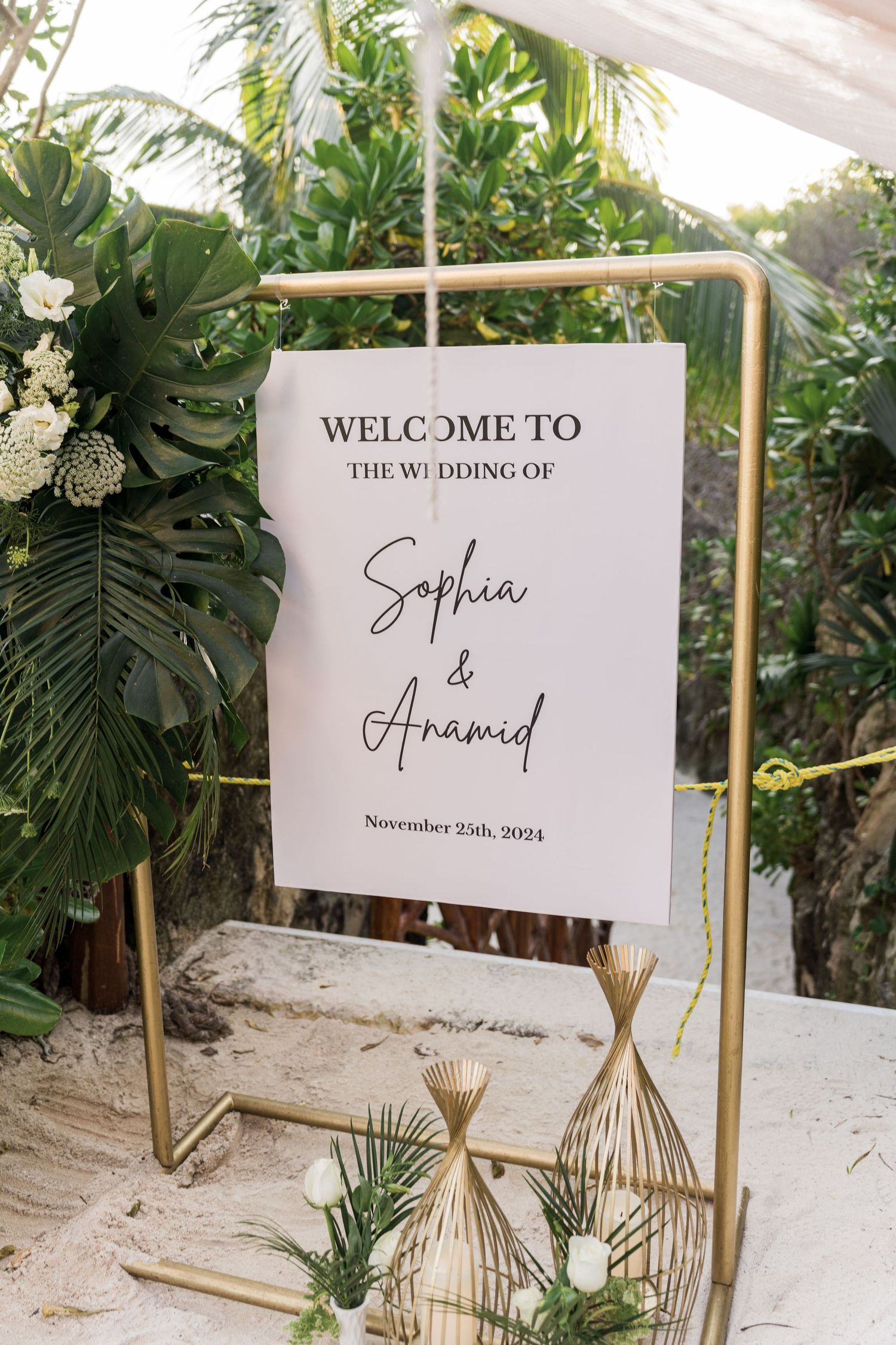 Xcaret Arte Wedding - Gold stand wedding welcome sign for Sophia & Anamid, November 25th 2024, surrounded by tropical greenery.