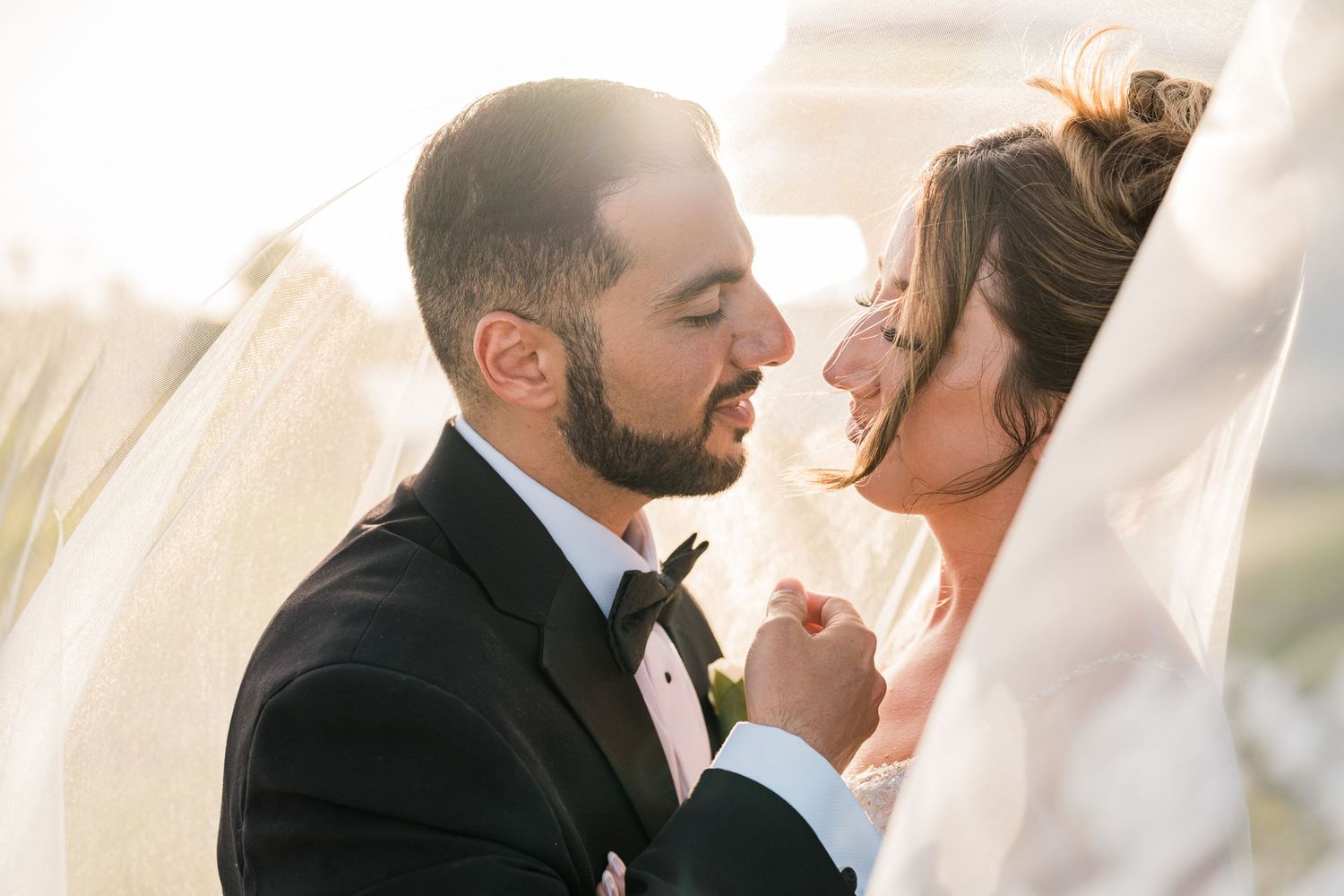 Bride and groom share a romantic moment holding hands under a flowing wedding veil.