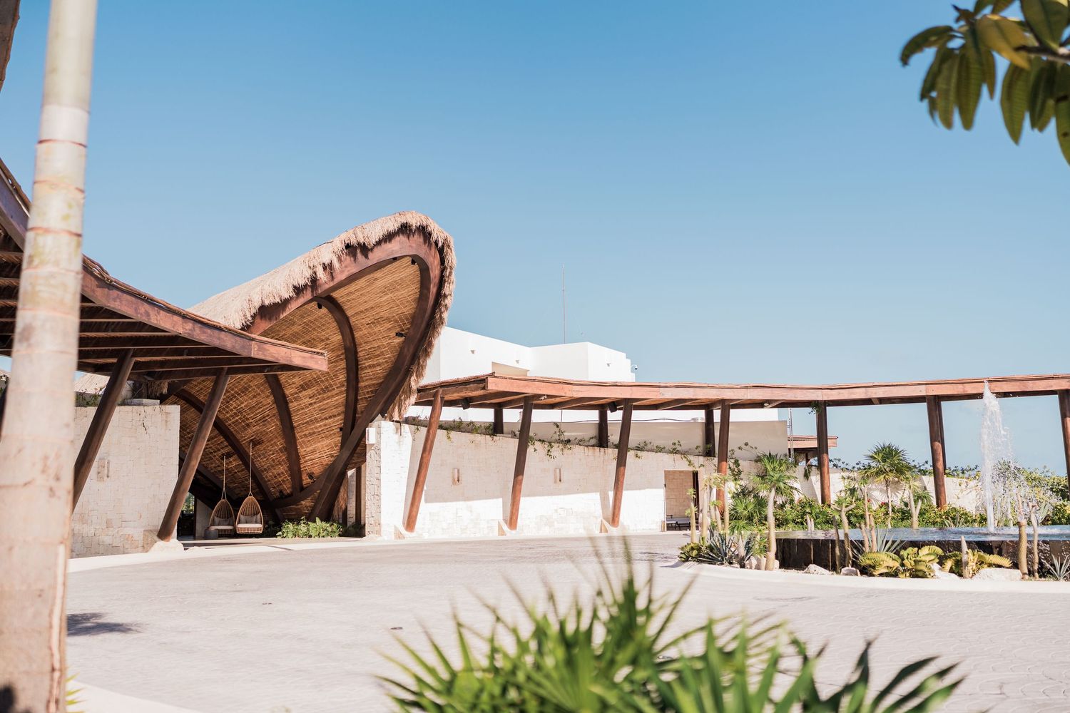 Stunning curved thatched-roof pavilion architecture at a luxury tropical resort under a clear blue sky.