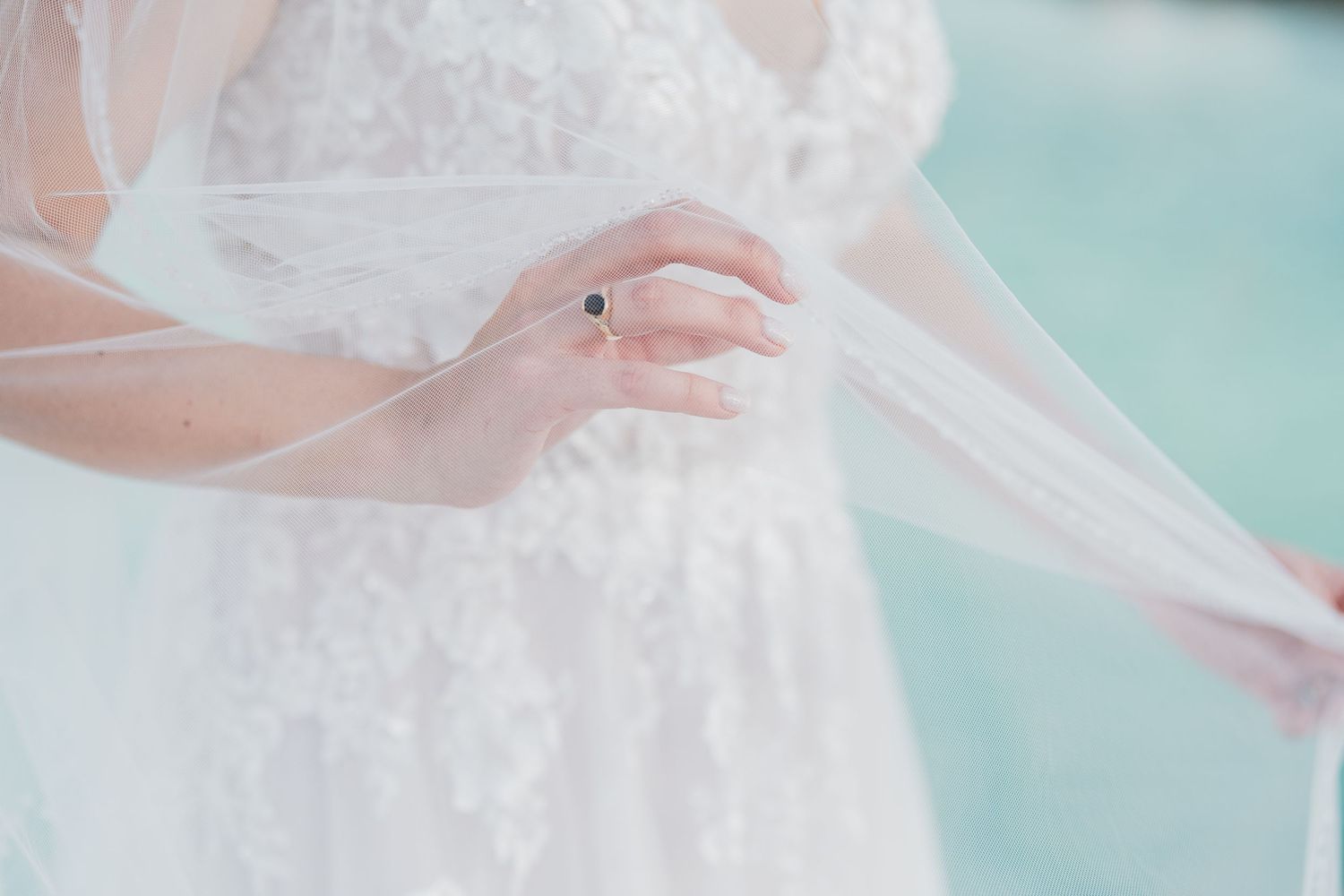Close-up of bride in lace wedding gown holding her veil with a sapphire ring on her finger.