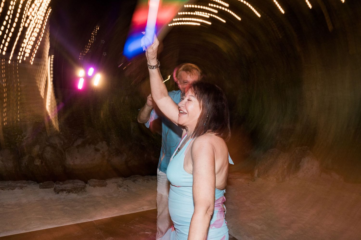Couple dancing joyfully under colorful lights in a tunnel venue at a festive nighttime event.