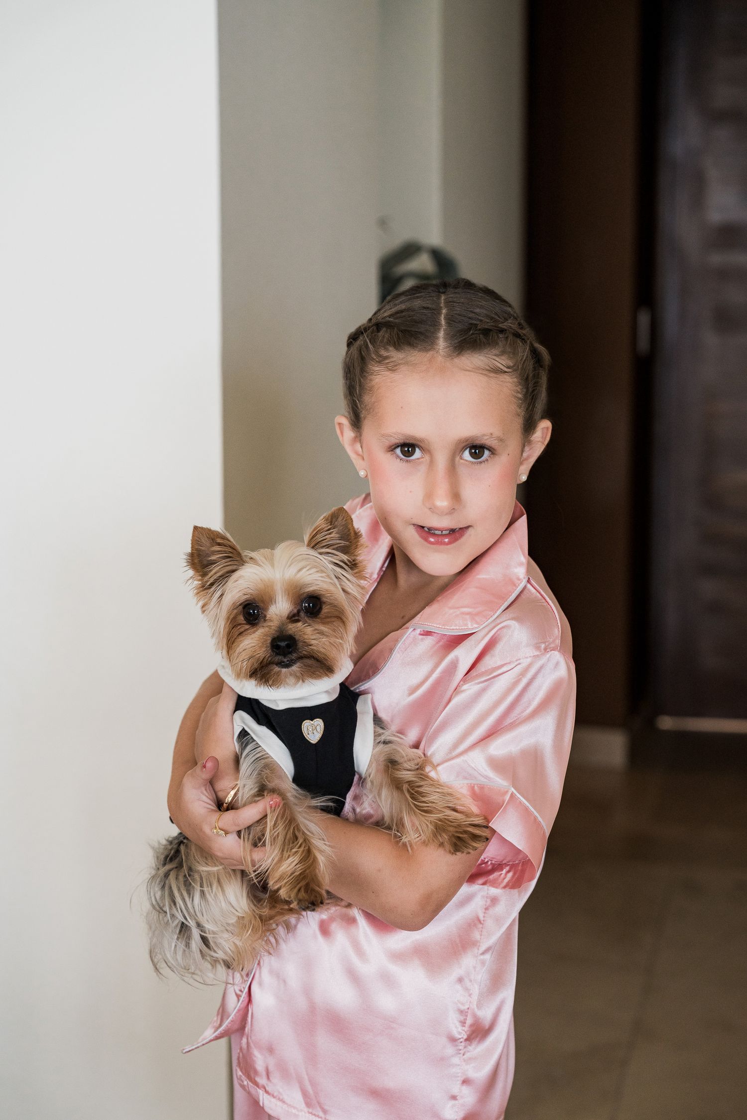 Young girl in pink satin robe holds a Yorkshire Terrier dressed in a black tuxedo outfit.